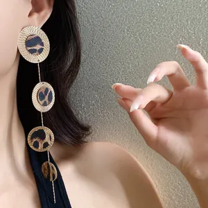 Détail rapproché de longues boucles d'oreilles léopard avec disques dorés texturés.
