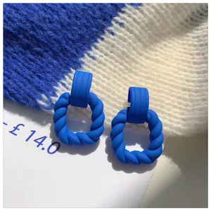 Macro detail of Klein blue matte twisted square hoop earrings on textured background.