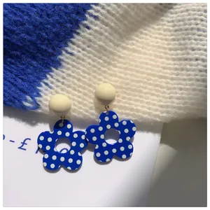 Close-up of Klein blue flower earrings with white polka dots on a soft knit background.