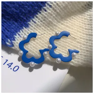 Close-up of Klein blue wavy flower hoop earrings with elegant white pearl accents