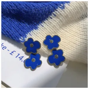 Close-up detail of Klein blue flower stud earrings with a sleek enamel finish