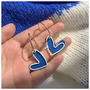 Detailed view of Klein Blue heart-shaped hoop earrings held on a hand