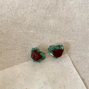 Close-up of green fabric heart earrings with cute brown resin bear details and silver needles.