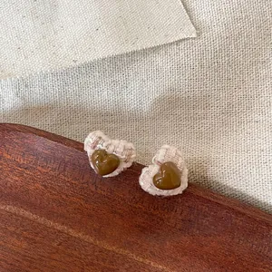 Macro view of heart-shaped stud earrings featuring brown resin and textured tweed fabric