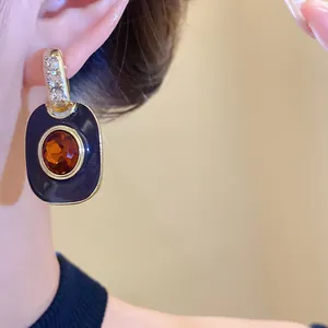 Detailaufnahme von Vintage-Emaille-Ohrringen mit bernsteinfarbenem Stein und Strass.