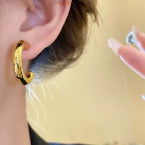 Close-up of minimalist gold polished C-shaped hoop earring worn on ear