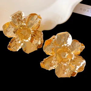 Close-up of golden metal pleated flower stud earrings with rich texture