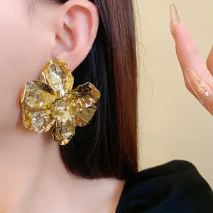 Macro view of a large gold metallic flower stud earring with textured petals on ear