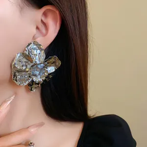 Close-up of large silver pleated flower stud earring worn on ear, high-shine metal.