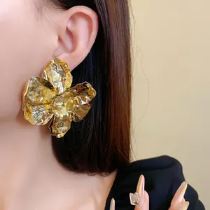 Close-up of a high-end golden metallic pleated flower stud earring on a model's ear