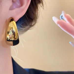 Close-up of a minimalist gold C-shaped earring with a high-shine metallic finish