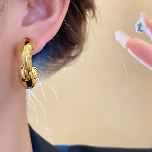 Close-up detail of textured C-shaped gold hoop earrings featuring a glossy minimalist finish