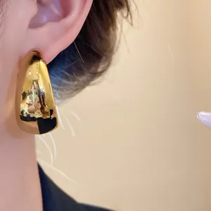 Detailed close-up of a golden minimalist C-shaped smooth stud earring on a person's ear