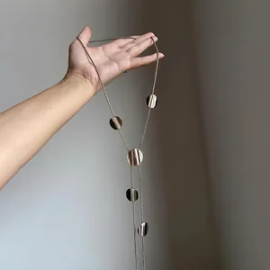 Primo piano di una collana lunga a Y con dischi circolari lucidi tenuta in mano.