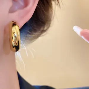 Detailed close-up view of a chunky gold C-shaped hoop earring worn on a model's ear