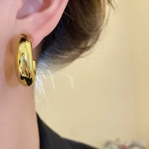 Detailed close-up view of chunky gold-plated C-shaped hoop stud earring worn on the ear