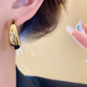 Macro detail of smooth C-shaped golden stud earring on ear with high metallic luster