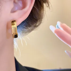 Close-up detail of minimalist golden smooth C-shaped hoop earring worn on a female ear