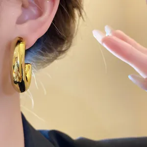 Close-up of a glossy gold C-shaped hoop earring worn on a model's ear.