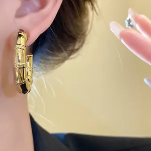 Detailed macro shot of golden bamboo joint C-shaped hoop earrings worn by a model