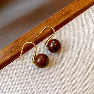 Detail shot of vintage-style brown bead gold hook earrings on a textured background.