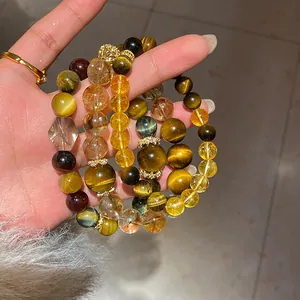 Stacked tiger eye and citrine stone beaded bracelets shown in a detailed hand-held shot