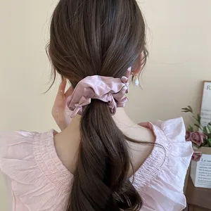 Close-up detail of a pink ruffled silk hair scrunchie with pearl accents on a ponytail
