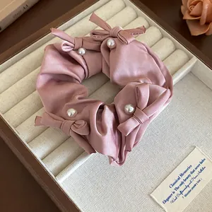 Detailed view of a pink satin scrunchie featuring chic bows and faux pearl accents