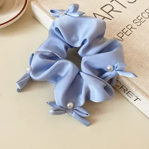 Detail of a light blue fabric scrunchie with cute bows and elegant pearl accents.