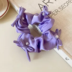 Close-up of a purple satin scrunchie featuring dainty bows and elegant pearl accents.
