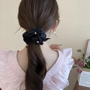 Close-up of a black ruffled fabric scrunchie with pearl accents on a ponytail