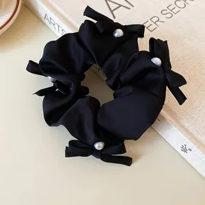 Close-up of an elegant black fabric scrunchie featuring delicate bows and white pearl beads.