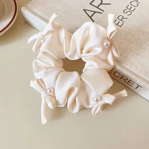 Close-up of elegant cream satin scrunchie with delicate bows and white pearls