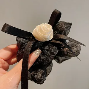 Detailed view of an elegant black fabric scrunchie with a cream rose and satin bow