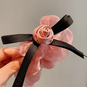 Close-up detail of a pink organza flower scrunchie featuring a satin rose and black bow