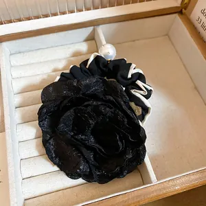 Detailed shot of a black fabric rose scrunchie with elegant white ruffles and a pearl accent