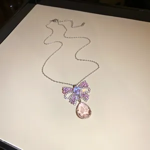 Nahaufnahme einer silbernen Halskette mit rosa Zirkon-Schleife und Tropfenanhänger