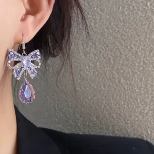 Nahaufnahme eines Zirkonia-Bogen-Ohrrings mit einem lila Kristallanhänger am Ohr getragen