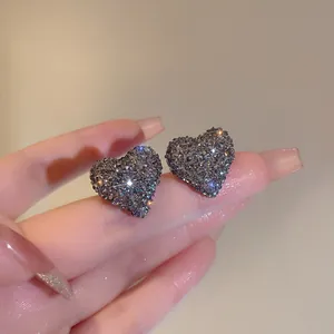 Primo piano dettagliato di orecchini a lobo a cuore con cristalli scintillanti sulle dita