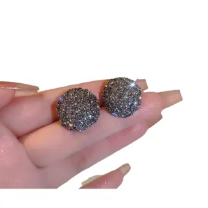 Eleganti orecchini a lobo in argento con strass grigi scintillanti sulla mano.