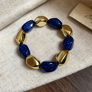 Dettaglio di un bracciale elastico vintage con perline dorate e blu glitterate.