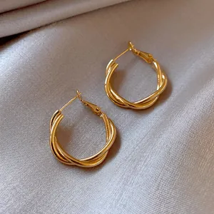 Detailed view of elegant gold-toned twisted hoop earrings on soft silk fabric.