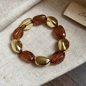 Dettaglio di un bracciale elastico retrò in acrilico ambra con perle dorate irregolari.