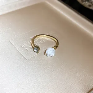 Detail shot of a gold-toned open ring with a white rose and a sparkling zircon