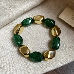 Dettaglio macro di un bracciale elastico vintage in acrilico con glitter verdi e perle oro