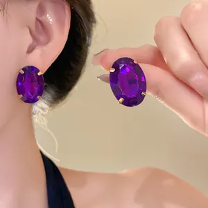 Close-up of elegant oval purple crystal stud earrings with gold-toned claw setting