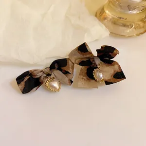 Detailed view of leopard print fabric bow earrings with elegant heart pearl pendants.