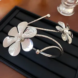 Primo piano di un bracciale a polsino con fiori argentati e strass su vassoio nero.