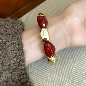 Dettaglio macro di un braccialetto elastico vintage con perle dorate e rosse acriliche