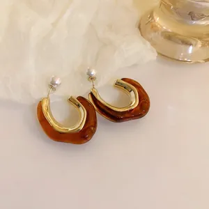 Macro detail of U-shaped Maillard style earrings featuring brown amber resin and pearls